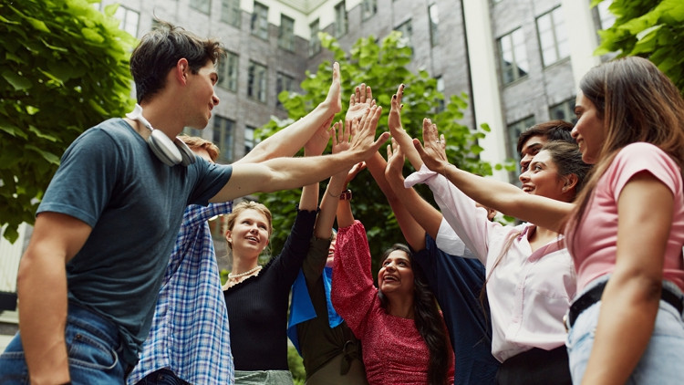 A group high-five among several post-secondary students outside a university building