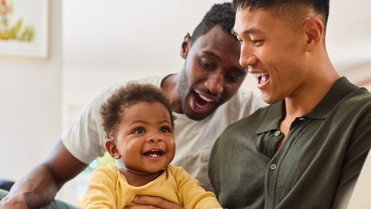 Two young dads, one holding baby on lap