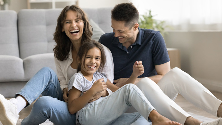 Young mother and father sitting on living room floor with young girl
