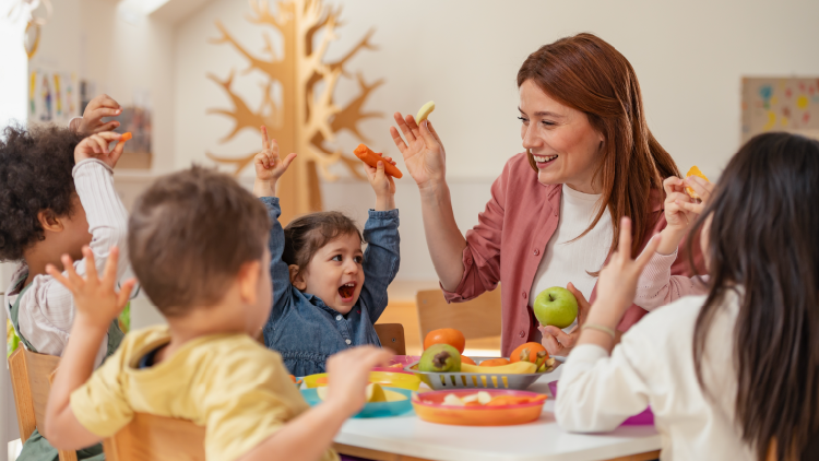 Woman sitting at a table with five children that are all eating fruits and vegetables