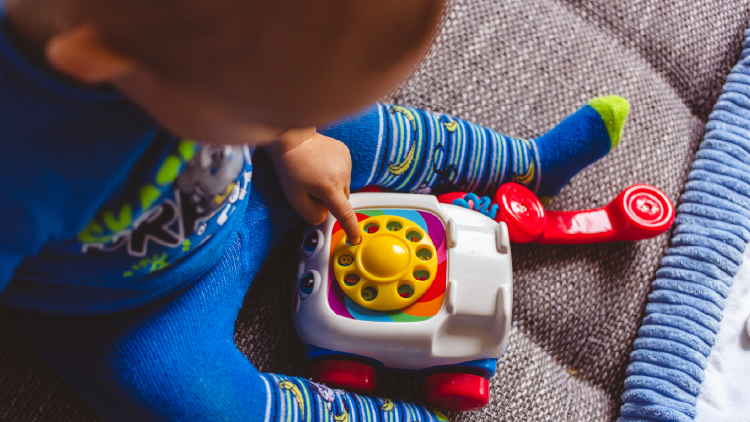 Young boy sitting on floor dialing a play old style rotary telephone