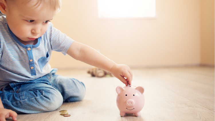 Baby boy sitting on floor putting loose change into a pink piggy bank