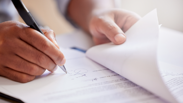 Person's hand writing on a document with a pen