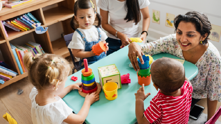 Woman sitting at a table with three young children playing with various toys
