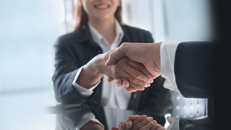 Two people shaking hands with a woman in the background