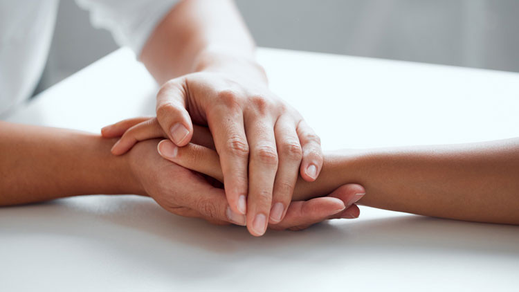 Close-up of one person gently holding another's hand in theirs, on a table