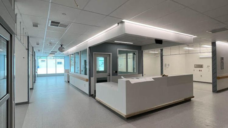Spacious, light-filled hospital corridor with closed patient rooms and a central nurses station.