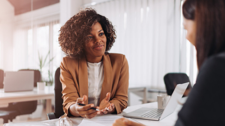 image of black woman at a desk, talking to another woman