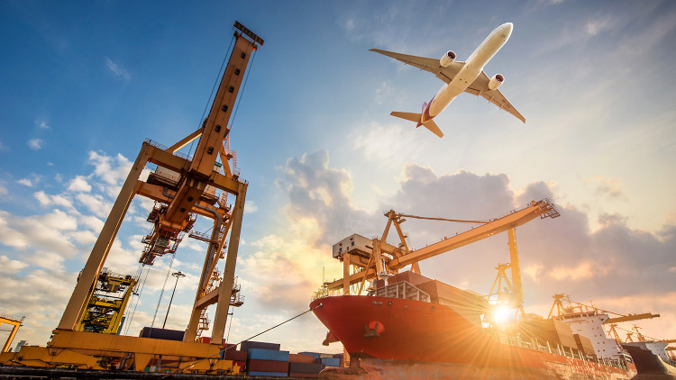 An airplane flies over a cargo ship at a harbour