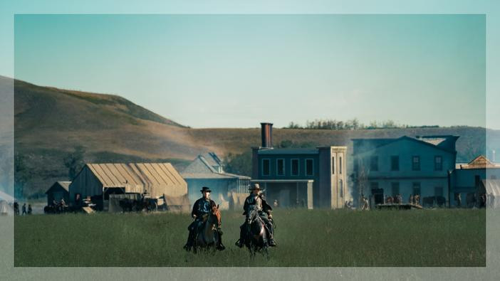 Two people riding on a horse with buildings in the background