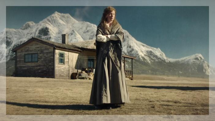 Woman standing with her eyes closed with a house and mountains in the background