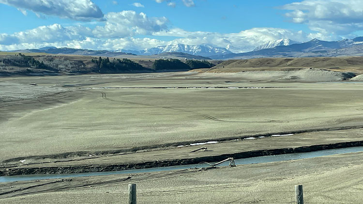 Cowley water intakes, Oldman River - River surrounded by flat green land with clouds and mountains in the background