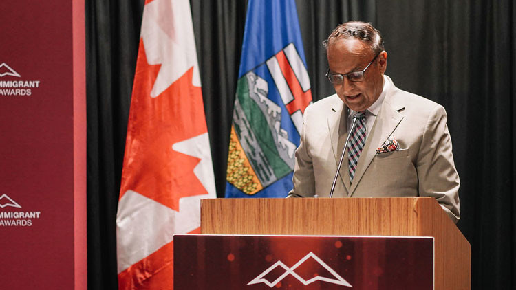 Associate Minister Yaseen speaking at the podium on stage at the 2025 Alberta Immigrant Impact Awards ceremony