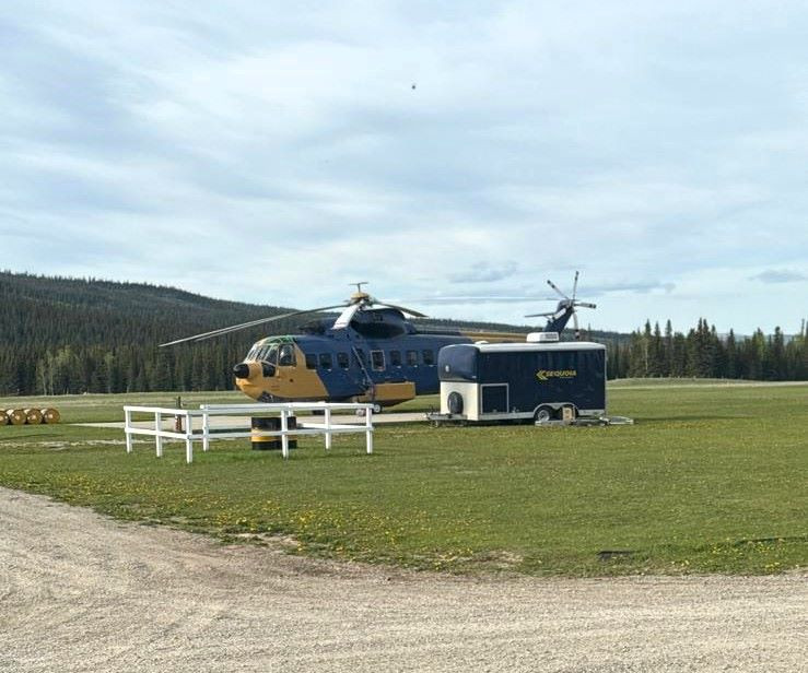 A heavy helicopter is sitting on a grass field with it's utility trailer next to it. 