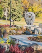 Indigenous reconciliation monument in a landscaped park, surrounded by rocks, plants, and autumn foliage.