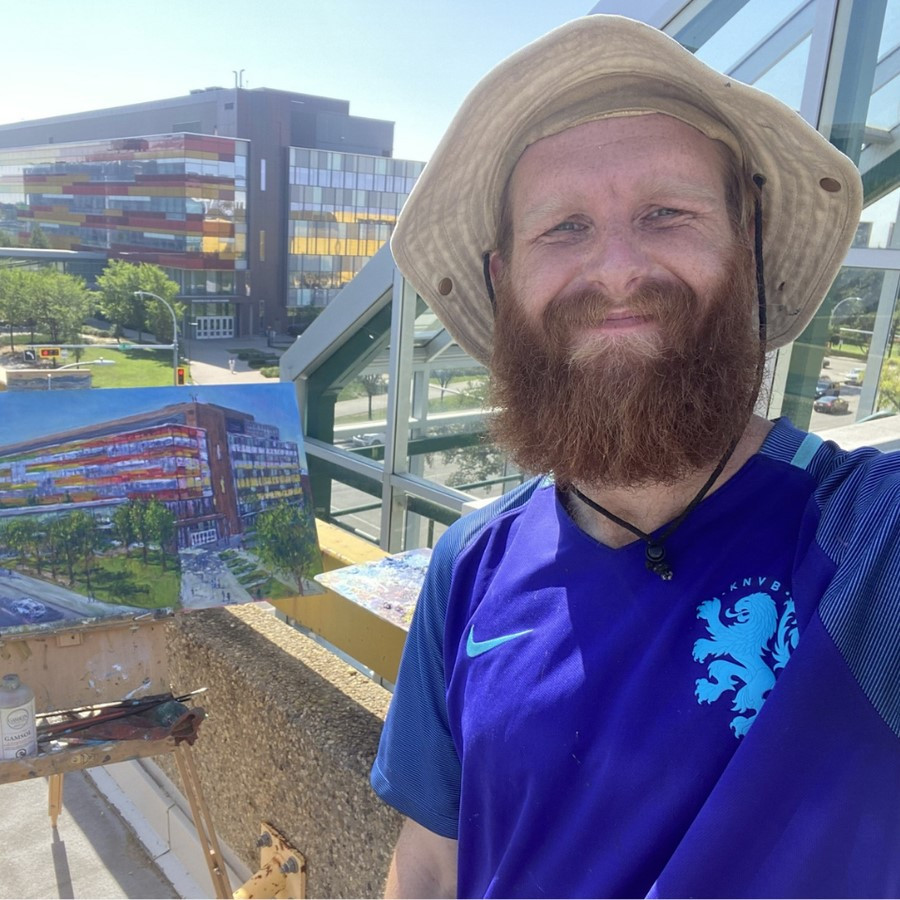 Nicholas Martin is beside his painting of a building, with the building in the background