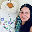 Sharon stands next to her beadwork on a white coat.