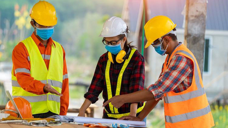 Three skilled trades workers are gathered around a table looking at blueprints.
