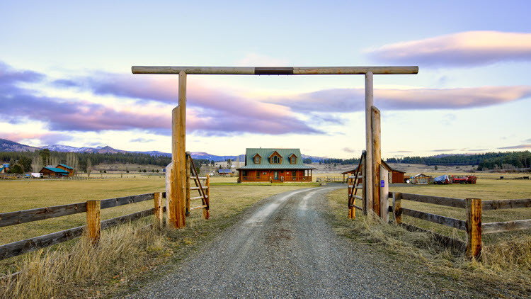 View of a farm house in the distance from the gravel driveway with a wooden gate