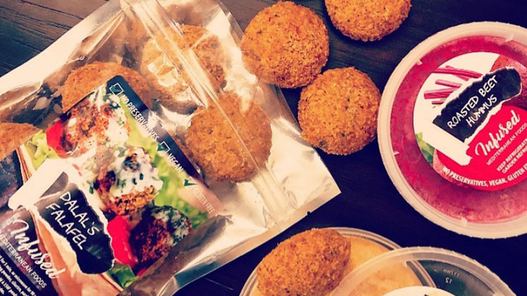 An open bag of falafels with falafels and containers of dip on a table