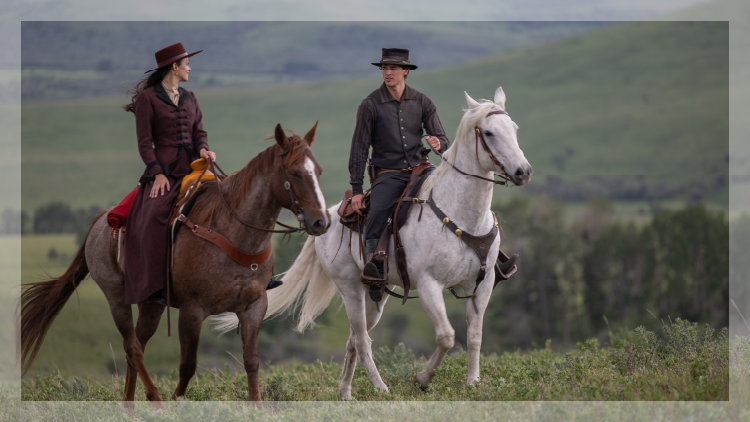 Cowboy and cowgirl each on a horse in a field with rolling hills in the background.
