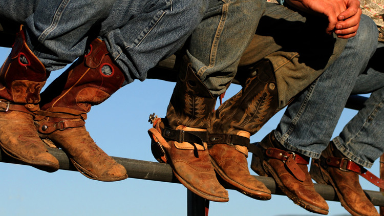 Three people sit on a fence wearing brown cowboy boots.