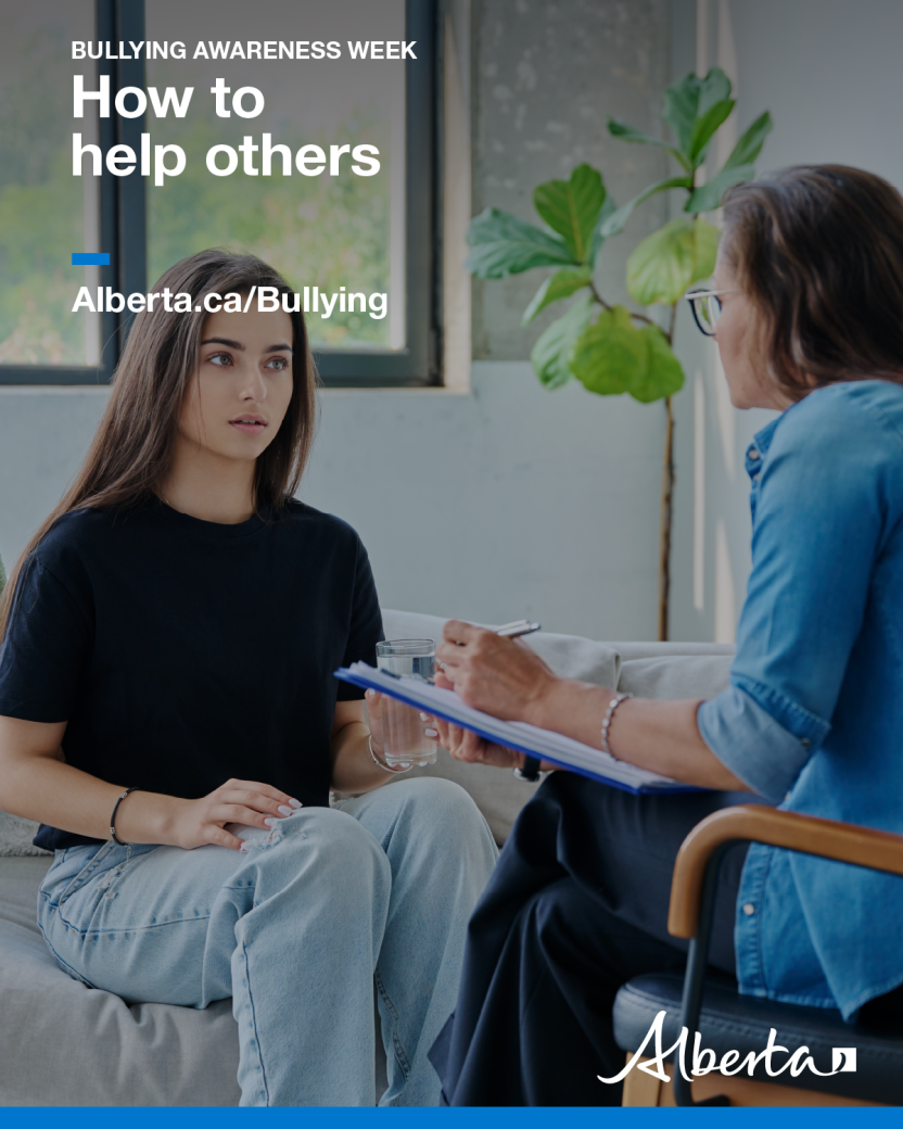Image of a young woman sitting while talking to a counsellor who is sitting across from her in a chair with a notepad and pen in her hand.