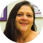 Kari Thomason smiles for the camera with photos in the background hanging on a wall.