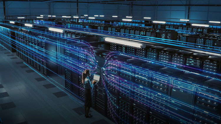 Woman stands in front of a large data centre with blue and purple lights coursing through the room.