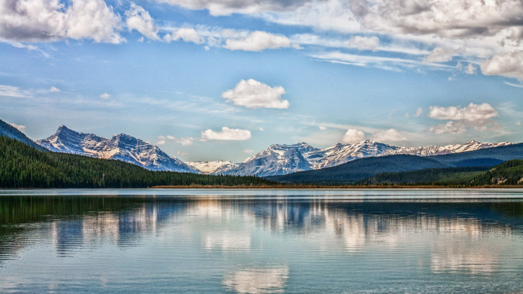 Photo on a lake with mountains and clouds reflecting in it.