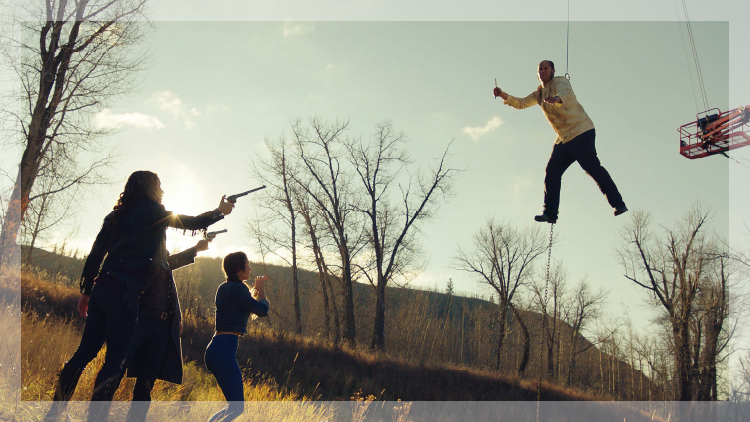 Production set: Person hanging in the air while 3 people are pointing guns at him