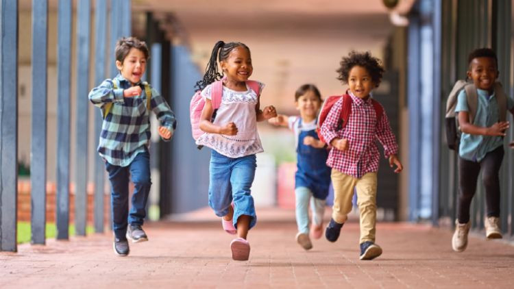 Group of multi-cultural elementary school pupils running along walkway outdoors at school.
