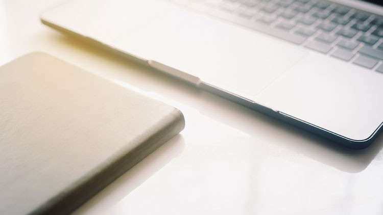 A laptop and notebook on a desk.