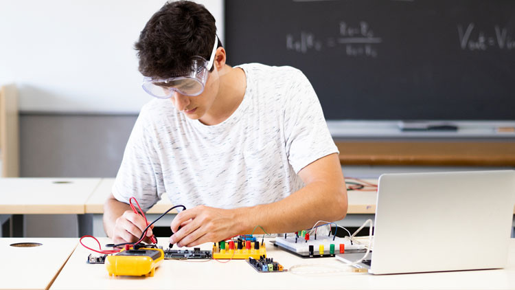 Student in a classroom with safety goggles on, working on electrical components