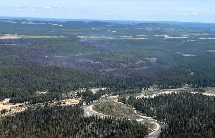 Very little smoke is hovering over the wildfire on the side of a slope.