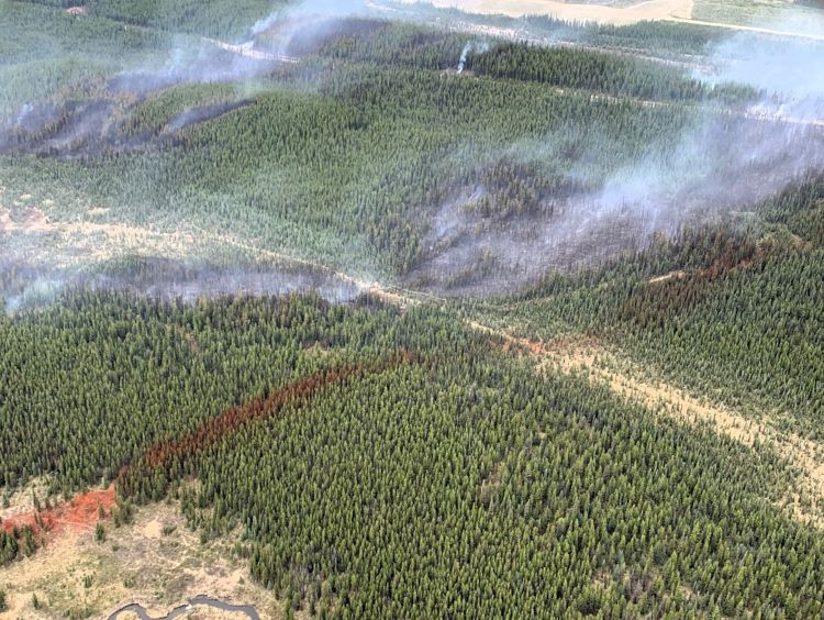 An overview of a wildfire with some low laying smoke and a red line of retardant over the trees. 