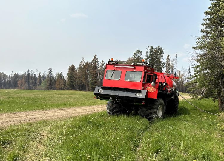 Water truck sits on the side of a gravel road with a hose hanging off the side.