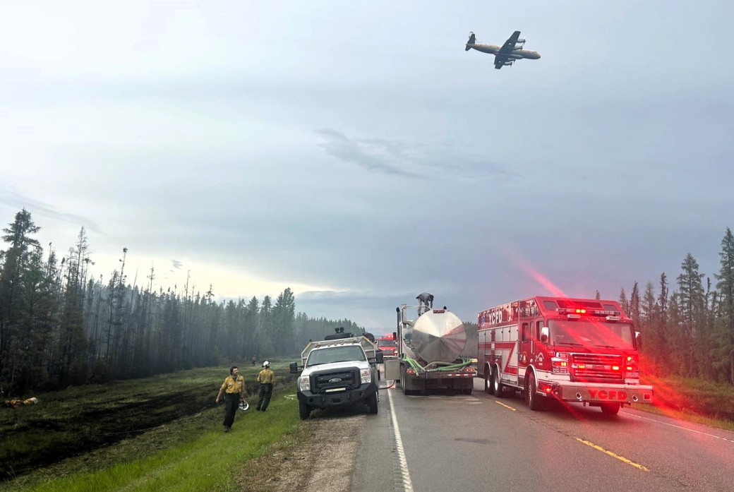 Fire engines, an airtanker plan and people standing on the side of the road assessing the wildfire.