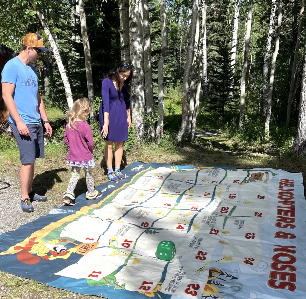 A family of three plays a giant board game in a park.