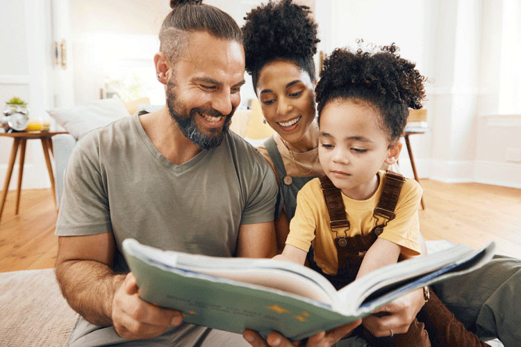 Mother, father and daughter sit on the floor reading a book together.