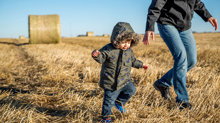 Mother and little son walking on the farm with hay bales at harvest time.