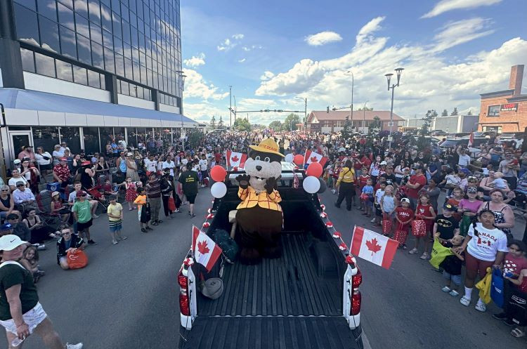 A large crowd lines the street during the Canada Day parade in Grande Prairie. Alberta Wildfire’s mascot, Bertie the Beaver, waves from the back of a decorated pickup truck with Canadian flags and balloons. 