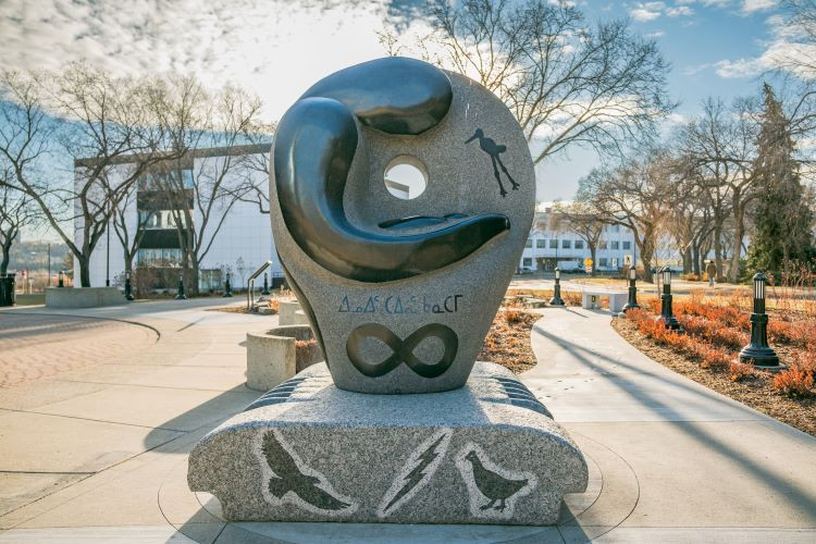 Photo of The Rock Grandmother side of the residential school monument, with a figure representing a woman holding an infant, with petroglyphs of a crane and symbols for the Inuit and Métis peoples.