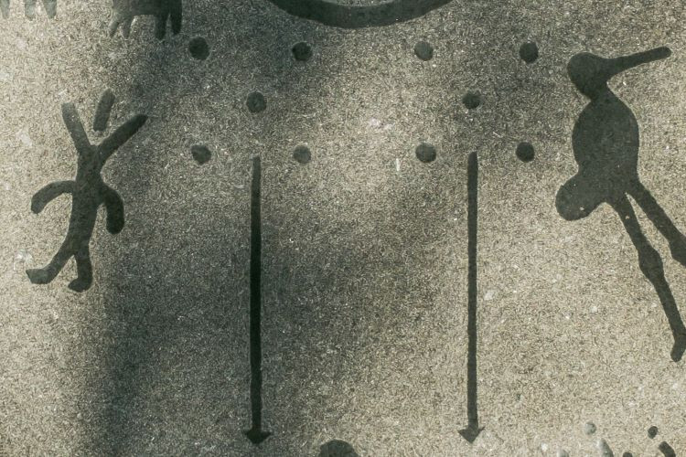 Photo of a petroglyph on the residential schools monument of two parallel roads with five posts above each line.