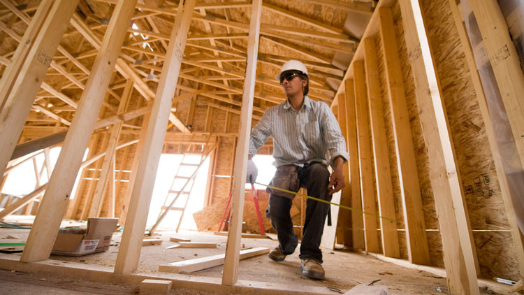 Construction worker with a hard hat holding a measuring tape in a wood framed structure under construction