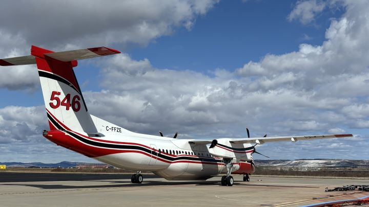 A firefighting aircraft is on the tarmac at an airport with cloudy blue skies in the background.