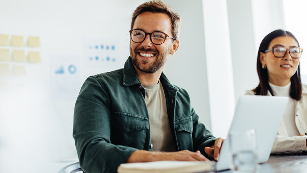 Smiling man and woman using their laptops, sitting at a table