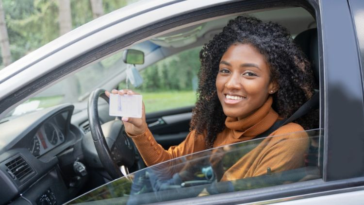 Female driver smiling and holding a driver's licence.