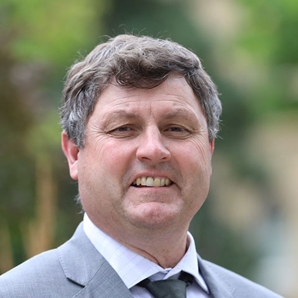 Rick Wilson poses, smiling at the camera, wearing a light grey suit and black tie.